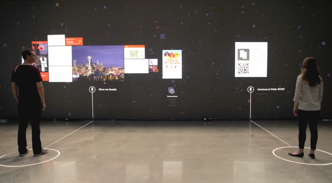 Two people stand at separate floor markers in front of one wall projection, with different information panels beside each person.