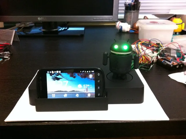 An Android robot prototype beside a docked Nexus phone, with its wiring still exposed.
